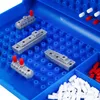 A close-up view of a Battleship board game with gray ship pieces and red and white pegs on a blue grid. Produktbild-Vorschau
