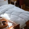 A white comforter is laid out on a bed, with sunlight streaming across it. A woven tray with a bowl is in the foreground. Produktbild-Vorschau