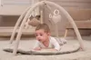 A baby is lying on a play mat under a play gym. Produktbild-Vorschau