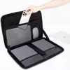A hand is placing a smartphone into a laptop bag that is open, revealing compartments for a laptop and accessories. Another laptop is visible in the background. Produktbild-Vorschau