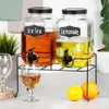 Two glass beverage dispensers with spigots on a black metal stand, with a glass of amber liquid and fruit slices visible. Náhľad obrázku produktu