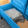 A blue wooden garden bench with its lid open, revealing a folded gray blanket inside. The bench is placed on a paved patio. Anteprima dell’immagine prodotto