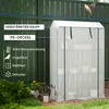A small greenhouse with shelves, filled with potted plants, is set up outdoors next to a green fence. Produktbild-Vorschau