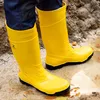 A person wearing yellow rubber boots standing in mud and puddles. Produktbild-Vorschau