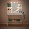 A white vanity table with a lighted mirror, drawers, and shelves, displaying various makeup and beauty products. Produktbild-Vorschau