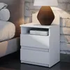A white bedside table with two drawers and an open shelf, next to a bed. Náhľad obrázku produktu