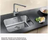 A stainless steel kitchen sink with a modern faucet is shown on a dark countertop, with some food items and a bowl of salad nearby. Produktbild-Vorschau