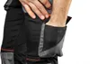 A close-up shot of a person's hand reaching into the pocket of black work pants with gray accents and orange stitching. Náhled obrázku produktu