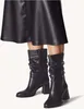 A pair of black leather slouch boots worn with a black leather skirt. Podgląd zdjęcia produktu