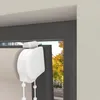 A close-up view of a white roller blind mechanism attached to a window frame. The window shows a blurred background of trees with autumn foliage. Produktbild-Vorschau