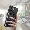 A hand holding a black phone case with a ring holder and camera cover, with a blurred indoor background. Produktbild-Vorschau