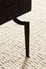 A close-up of a dark wooden table leg with a metallic cap, resting on a textured beige rug. Anteprima dell’immagine prodotto
