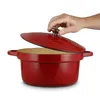 A person's hand is lifting the lid of a red Dutch oven. Podgląd zdjęcia produktu