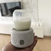A hand holding a portable bottle warmer with a bottle of milk on top, in a home setting. Produktbild-Vorschau