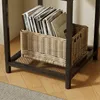 A close-up view of the lower section of a side table, featuring a woven basket filled with magazines and books. Produktbild-Vorschau