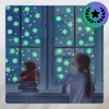A child looks out a window decorated with glowing snowflakes, with a teddy bear on a stack of books on the windowsill. Podgląd zdjęcia produktu