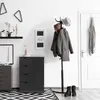 An entryway scene with a black wooden cabinet, a coat rack with coats and a hat, a door, and a rug. Podgląd zdjęcia produktu