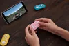 A person is holding a pink gamepad while playing a racing game on a smartphone, with other gamepads visible. Náhľad obrázku produktu