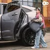 A young girl is carrying a car seat next to an open car door. Produktbild-Vorschau