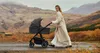 A woman pushes a stroller through a scenic, autumnal landscape. Produktbild-Vorschau