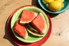 Watermelon slices on a plate next to lemons in a bowl, on a wooden table. Náhled obrázku produktu