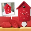 A red cuckoo clock is displayed on a couch with red pillows. Produktbild-Vorschau