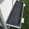 A close-up view of a black plastic tray with a textured surface, part of a grey and white animal hutch, set against a background of green grass and white wooden panels. Produktbild-Vorschau