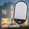 A modern LED outdoor light with a motion sensor is shown in front of a blurred house at dusk. Produktbild-Vorschau