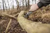 A person is using a folding saw to cut a fallen branch in a wooded area. Produktbild-Vorschau