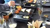 Menschen versammeln sich um einen Tisch und bereiten mit dem ausziehbaren Raclette-Grill von Unold B Produktbild-Vorschau