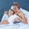 A mother and daughter are in bed, with the mother reading to the daughter. Produktbild-Vorschau