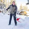 A man is shoveling snow in a snowy environment with trees and a house in the background. Náhled obrázku produktu