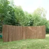 A woven reed fence is displayed in a grassy outdoor setting with trees in the background. Náhled obrázku produktu
