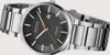 A close-up, studio shot of a men's wristwatch with a dark dial and a metal band. Náhled obrázku produktu