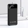 A black power bank is charging from a white power adapter plugged into a white power strip. The power bank has a digital display showing 100%. Produktbild-Vorschau