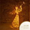 A lighted angel decoration with a trumpet against a stone wall. Voir les images du produit
