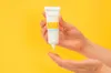 Hands holding a tube of sunscreen against a yellow background. Náhled obrázku produktu