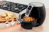 A person using a black air fryer filled with french fries, with potatoes and dipping sauces on a cutting board and a gas stove in the background. Anteprima dell’immagine prodotto