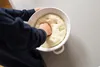 A person's hands are punching down dough in a white bowl. Produktbild-Vorschau