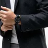 A close-up shot of a person wearing a dark patterned jacket and a black watch on their wrist. Podgląd zdjęcia produktu