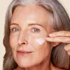A close-up of a woman applying cream to her face. Anteprima dell’immagine prodotto