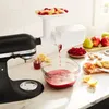 A KitchenAid stand mixer with a juicer attachment is shown in a kitchen setting, juicing fruits and berries into a glass bowl. Voir les images du produit