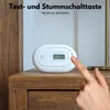 A hand is pressing a button on a white carbon monoxide detector placed on a wooden nightstand. Produktbild-Vorschau