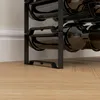 A close-up view of a black metal wine rack holding several wine bottles, resting on a light brown wooden floor. Náhled obrázku produktu