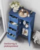 A blue bathroom cabinet with drawers and a door open, displaying various toiletries and accessories. A vase of flowers is on top. Produktbild-Vorschau