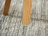Close-up of a wooden chair leg with a white floor protector on a textured rug. Voir les images du produit