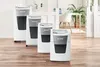 Four paper shredders are lined up in a row on a wooden floor in an office setting. Voir les images du produit