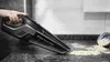 A hand holding a black handheld vacuum cleaner, cleaning up spilled food on a kitchen counter. Podgląd zdjęcia produktu