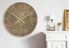 A round, decorative wall clock with a sunburst pattern is mounted on a white wall above a white fireplace mantel. A small lamp and a potted cactus are on the mantel. Náhľad obrázku produktu