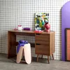 A desk with drawers, a stool, and artwork in a room with a grid-patterned wall. Produktbild-Vorschau